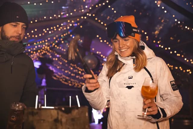 Feestende gast met een spritz in de verlichte kastent van de Après Ski Hideout